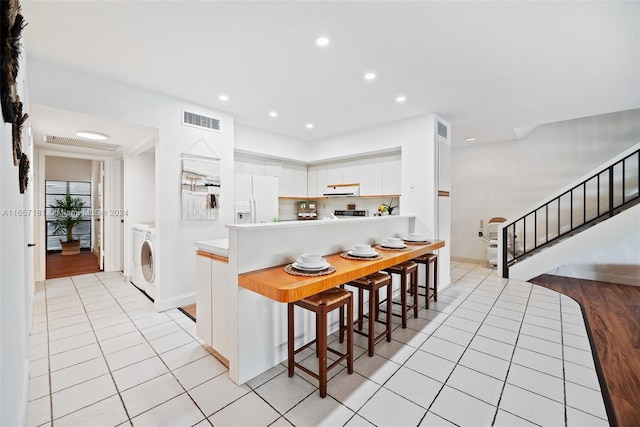 kitchen featuring kitchen peninsula, extractor fan, white cabinetry, white refrigerator with ice dispenser, and a kitchen bar