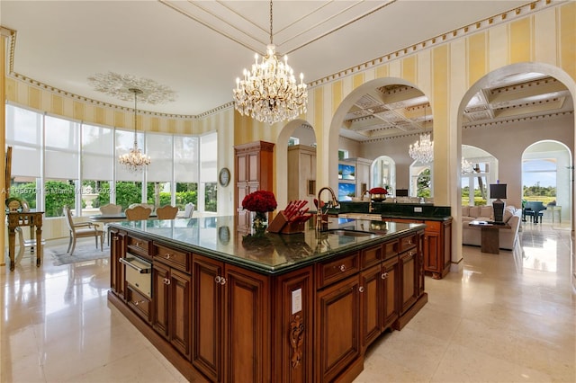 kitchen featuring coffered ceiling, decorative light fixtures, an inviting chandelier, an island with sink, and sink