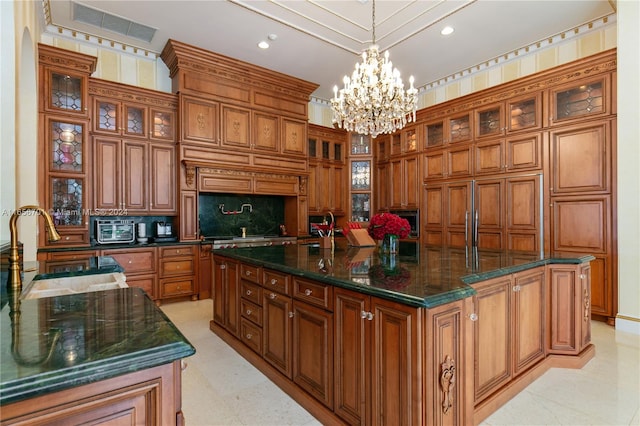 kitchen featuring dark stone countertops, pendant lighting, an inviting chandelier, sink, and a center island with sink