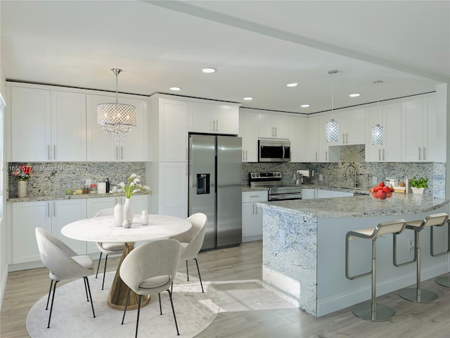 kitchen with white cabinetry, light hardwood / wood-style flooring, light stone counters, hanging light fixtures, and appliances with stainless steel finishes