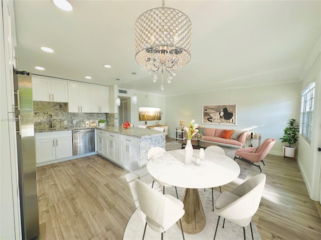 dining space featuring ornamental molding, light hardwood / wood-style flooring, sink, and a notable chandelier