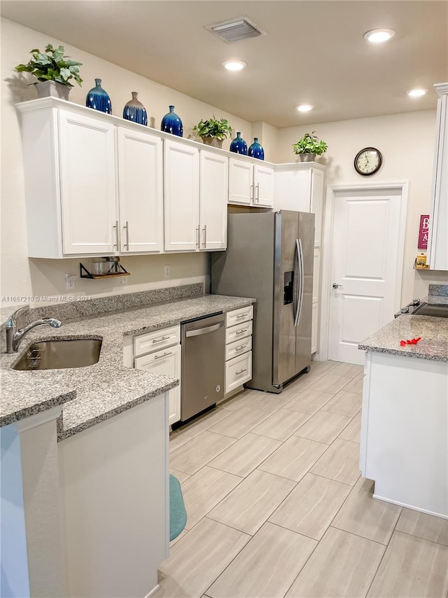 kitchen with light stone counters, sink, appliances with stainless steel finishes, and white cabinetry