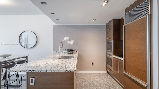 kitchen with built in appliances, a kitchen bar, kitchen peninsula, sink, and light stone countertops