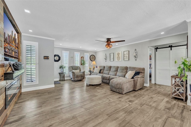 living room with a textured ceiling, a barn door, ceiling fan, and light wood-type flooring