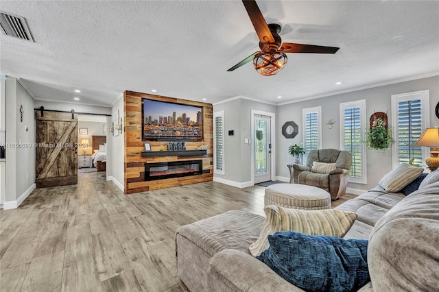 living room featuring light wood-type flooring, crown molding, a textured ceiling, ceiling fan, and a barn door