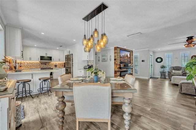 dining room featuring light wood-type flooring, ceiling fan with notable chandelier, a textured ceiling, and ornamental molding