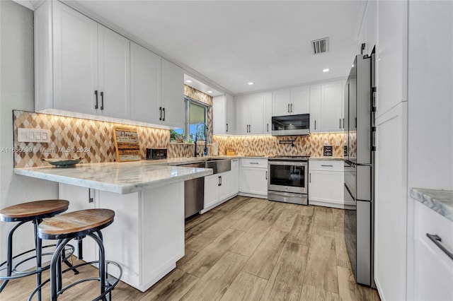 kitchen with white cabinetry, light hardwood / wood-style flooring, a kitchen bar, stainless steel appliances, and light stone counters