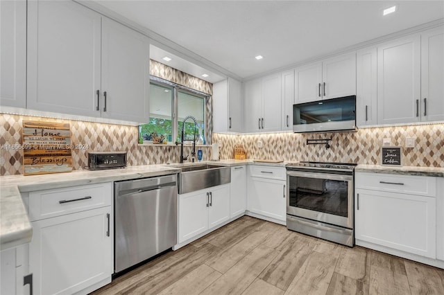 kitchen with sink, appliances with stainless steel finishes, white cabinetry, and light hardwood / wood-style floors