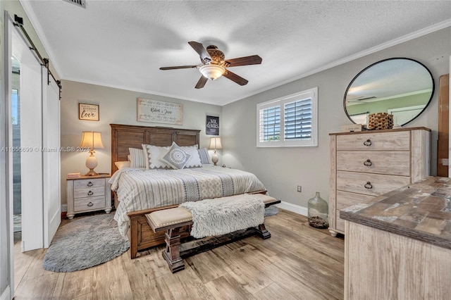 bedroom featuring crown molding, a barn door, light hardwood / wood-style floors, ceiling fan, and a textured ceiling