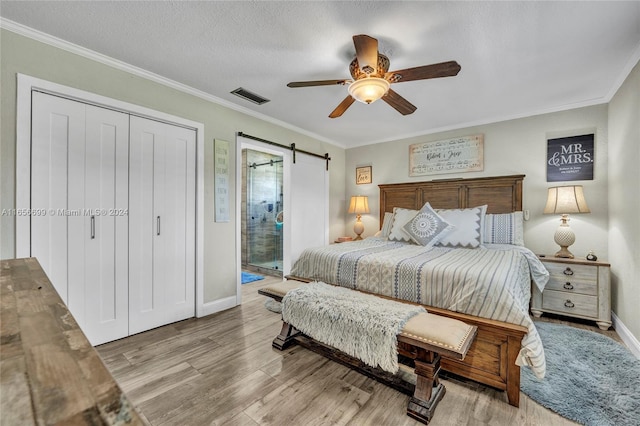 bedroom featuring a barn door, ceiling fan, light hardwood / wood-style floors, and ornamental molding