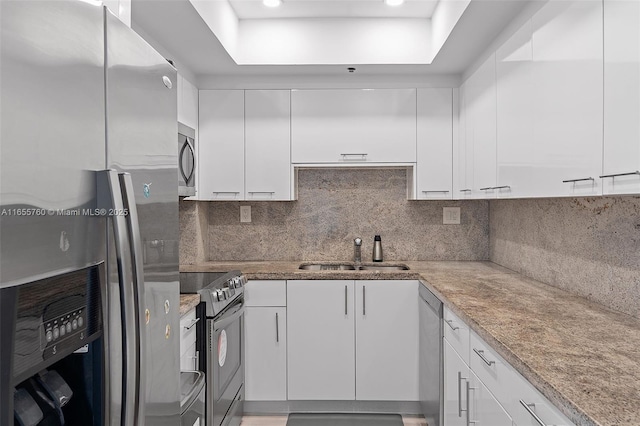 kitchen featuring decorative backsplash, light stone countertops, stainless steel appliances, white cabinetry, and a sink