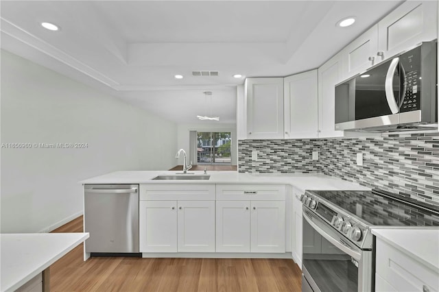 kitchen with appliances with stainless steel finishes, sink, decorative backsplash, light wood-type flooring, and white cabinets