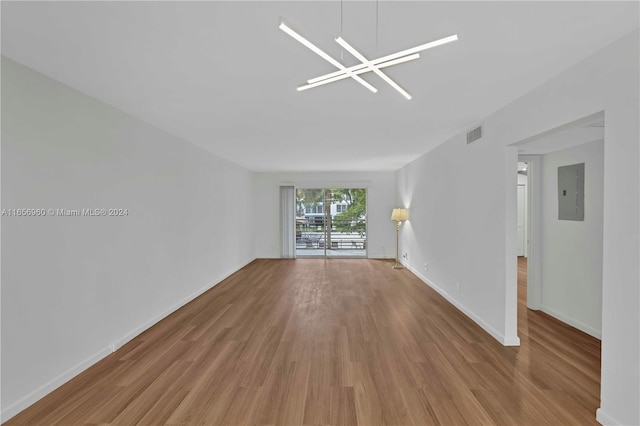 spare room featuring electric panel, light wood-type flooring, and a chandelier