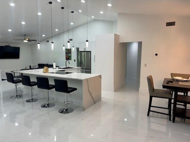 kitchen with a large island with sink, stainless steel fridge, a kitchen bar, ceiling fan, and hanging light fixtures