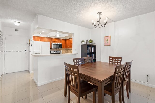 tiled dining area with a textured ceiling, ceiling fan with notable chandelier, and a tray ceiling