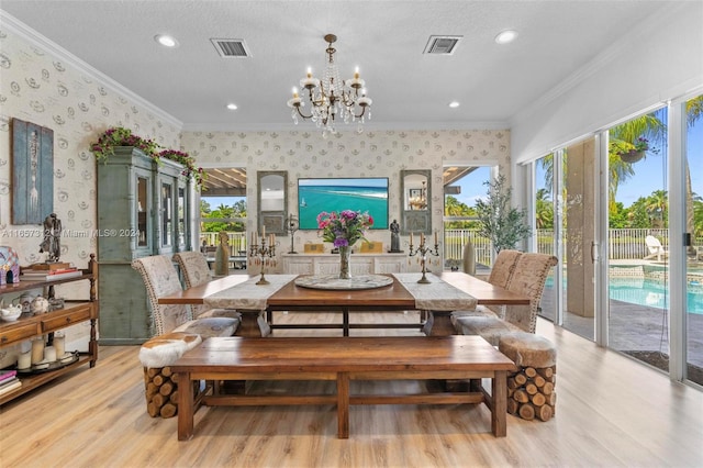 dining room with light wood-type flooring, an inviting chandelier, a textured ceiling, and ornamental molding