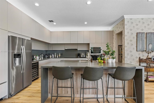 kitchen with light hardwood / wood-style floors, stainless steel appliances, wine cooler, and a kitchen island with sink