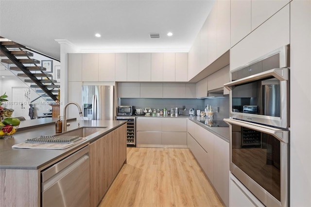 kitchen with appliances with stainless steel finishes, light hardwood / wood-style floors, sink, decorative backsplash, and ornamental molding