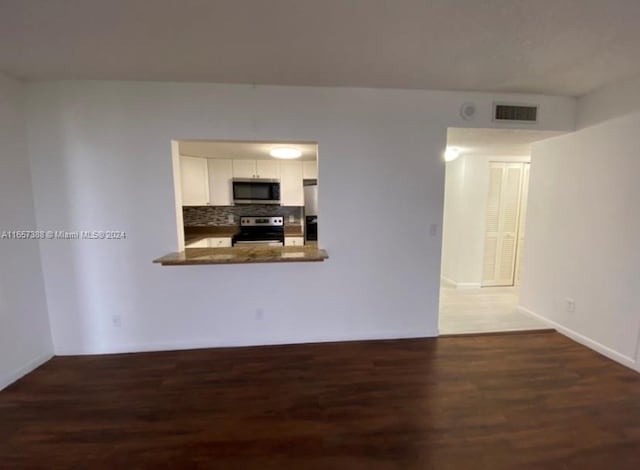 kitchen featuring white cabinetry, kitchen peninsula, dark wood-type flooring, decorative backsplash, and appliances with stainless steel finishes