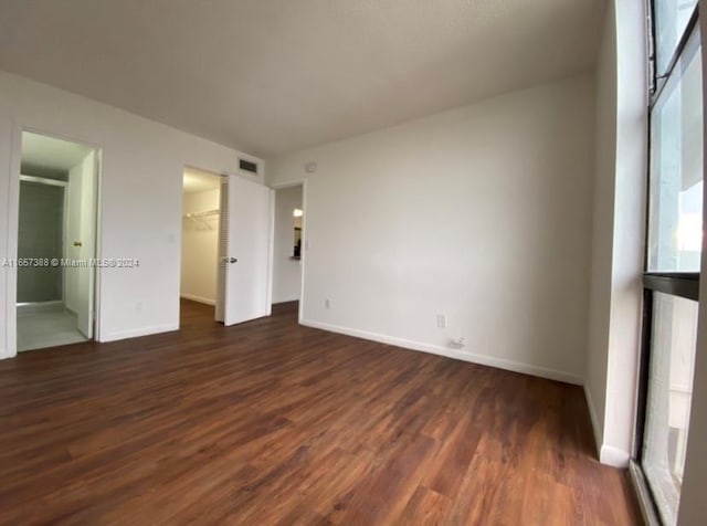 unfurnished bedroom with dark wood-type flooring, a walk in closet, and a closet