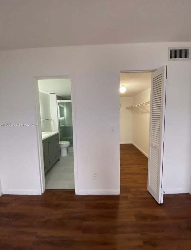 unfurnished bedroom with a walk in closet, dark hardwood / wood-style flooring, connected bathroom, and a closet