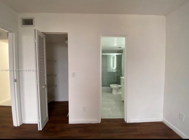 unfurnished bedroom featuring dark hardwood / wood-style flooring, ensuite bathroom, and a closet