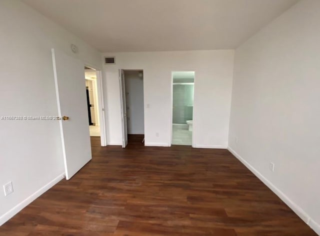 unfurnished bedroom featuring ensuite bathroom and dark hardwood / wood-style flooring