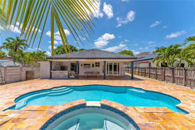 view of swimming pool featuring a pool with connected hot tub, french doors, a fenced backyard, and a patio area