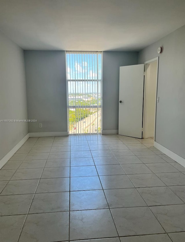 empty room featuring a wall of windows and light tile patterned floors