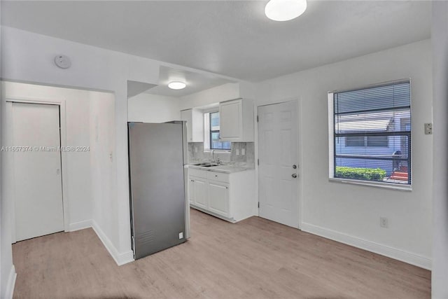 kitchen featuring white cabinets, light countertops, freestanding refrigerator, light wood-type flooring, and baseboards