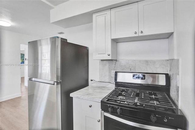 kitchen with hardwood / wood-style flooring, light stone counters, stainless steel appliances, and white cabinets