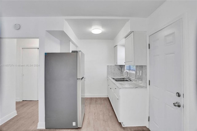 kitchen featuring white cabinets, a sink, freestanding refrigerator, light wood-style floors, and light countertops