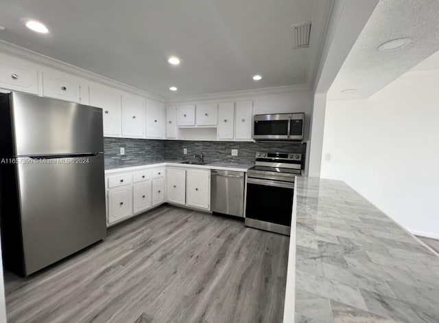 kitchen with white cabinets, appliances with stainless steel finishes, tasteful backsplash, and light hardwood / wood-style flooring