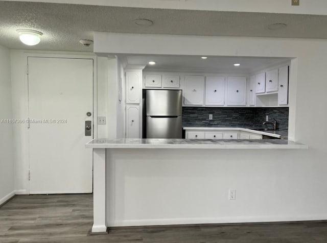 kitchen with kitchen peninsula, stainless steel fridge, and white cabinetry