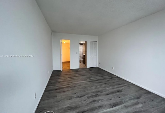 unfurnished bedroom with dark wood-type flooring, connected bathroom, and a closet