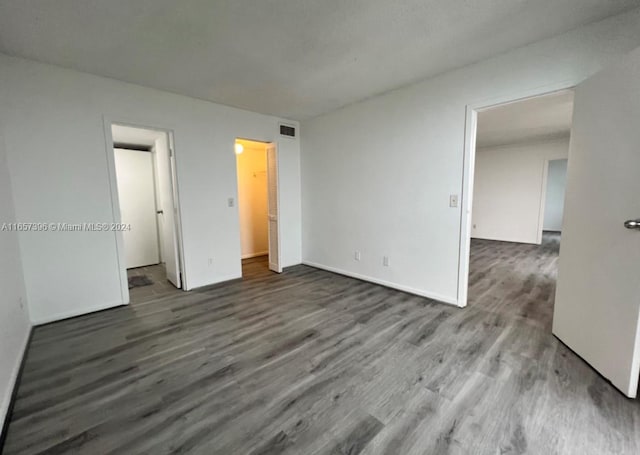 unfurnished bedroom featuring dark wood-type flooring, a walk in closet, and a closet