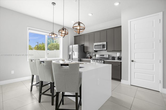 kitchen with pendant lighting, a kitchen breakfast bar, an island with sink, light tile patterned flooring, and stainless steel appliances