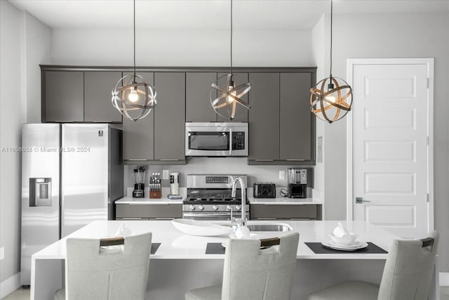 kitchen featuring appliances with stainless steel finishes, decorative light fixtures, gray cabinets, and a kitchen breakfast bar