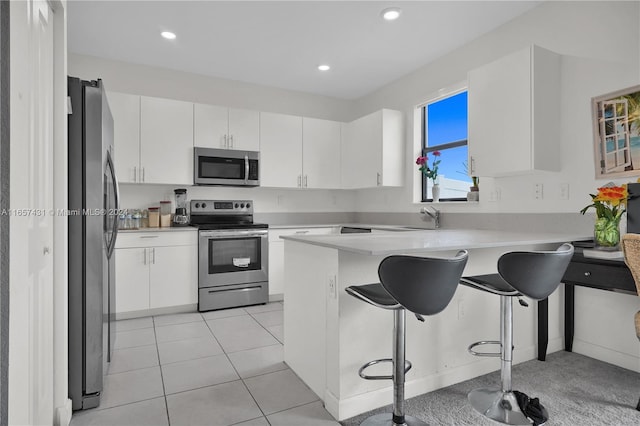 kitchen featuring white cabinetry, stainless steel appliances, kitchen peninsula, and a breakfast bar