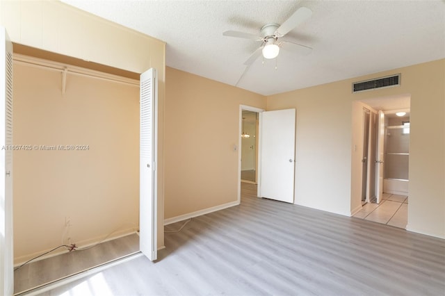 unfurnished bedroom with light hardwood / wood-style floors, a closet, a textured ceiling, ceiling fan, and ensuite bathroom