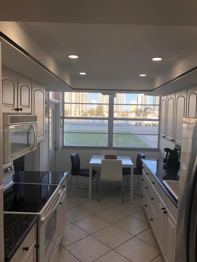 kitchen featuring light tile patterned floors, stainless steel appliances, dark stone counters, and white cabinetry