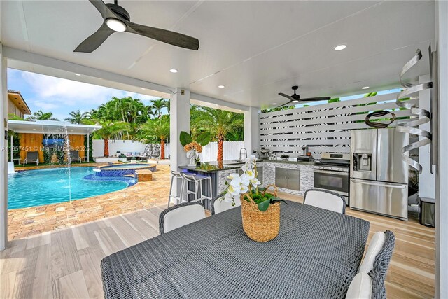 exterior space featuring ceiling fan, a wet bar, a pool with hot tub, pool water feature, and exterior kitchen