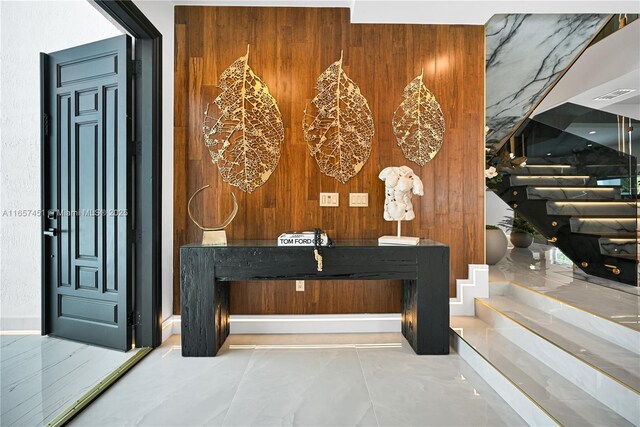 foyer with a chandelier, a raised ceiling, and wood walls