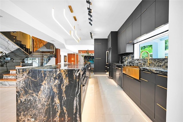 kitchen featuring tasteful backsplash, hanging light fixtures, light tile patterned floors, dark stone countertops, and stainless steel dishwasher