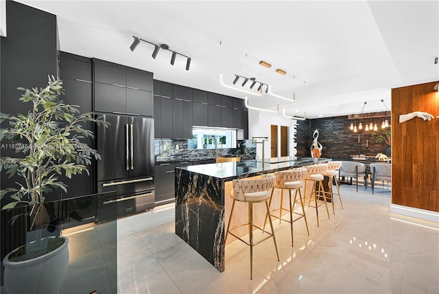 kitchen with a center island, high quality fridge, decorative backsplash, a kitchen bar, and decorative light fixtures