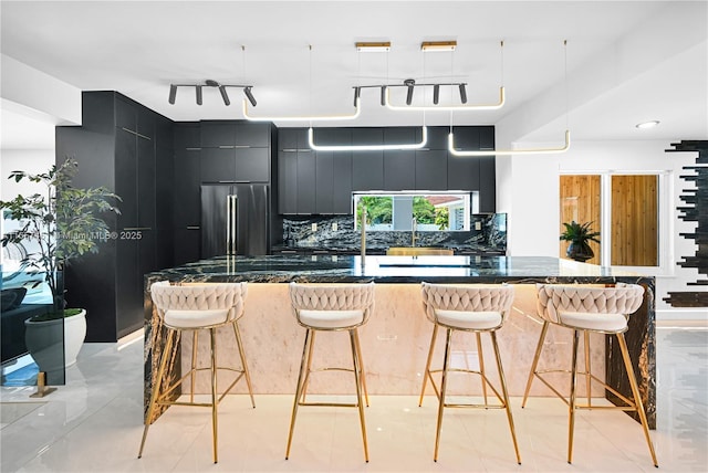 kitchen with sink, backsplash, track lighting, a kitchen bar, and high end refrigerator