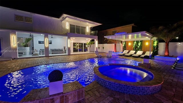 pool at night with ceiling fan, a patio area, and an in ground hot tub