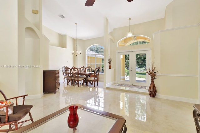 foyer featuring ceiling fan with notable chandelier, french doors, a healthy amount of sunlight, and a high ceiling