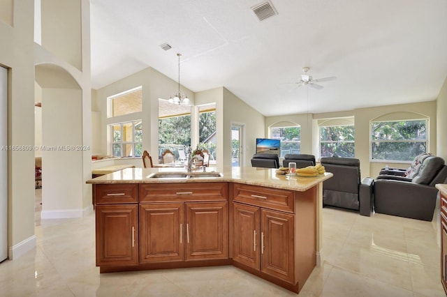 kitchen with a kitchen island with sink, ceiling fan with notable chandelier, light tile patterned floors, light stone counters, and sink