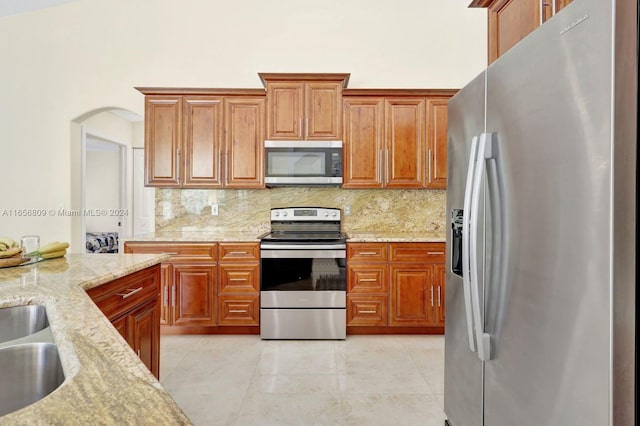 kitchen featuring light stone countertops, light tile patterned floors, stainless steel appliances, sink, and decorative backsplash